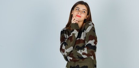 young lady in sweater, skirt holding hand on chin and looking merry , front view.